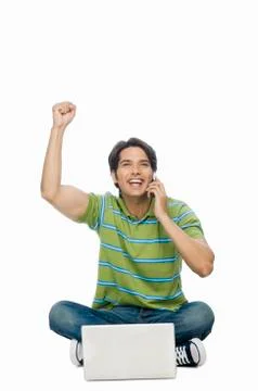 Young man using a laptop and talking on a mobile phone Stock Photos
