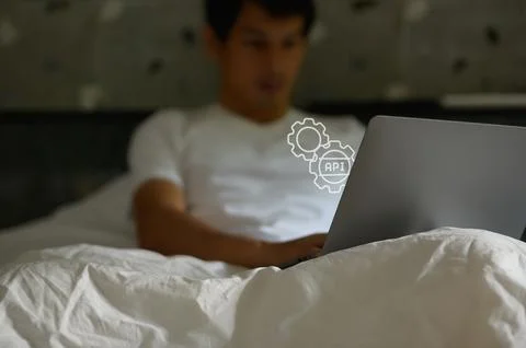 Young Man Using Laptop in Bed with API Concept Overlay Image Stock Photos