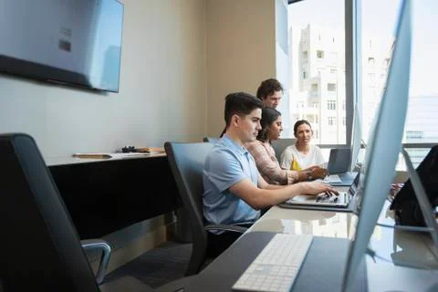 Young man using laptop computer in office conference room, co-workers having Foto stock