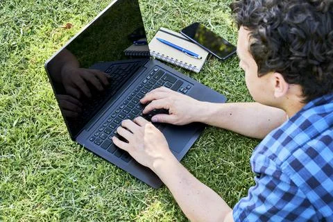 Young man using a laptop computer outdoors, on the grass, remote working Stock Photos