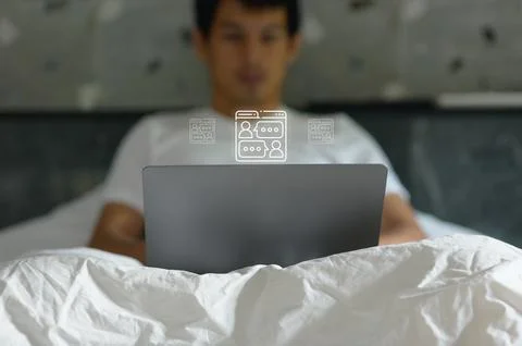 Young man using laptop computer in cozy bedroom with bed and wall decorations Stock Photos
