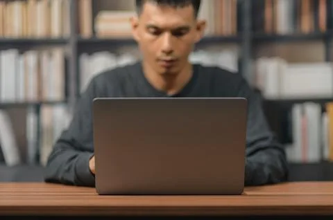 Young Man Using Laptop at Desk in Library with Bookshelves Background Stock Photos