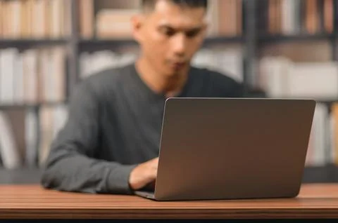 Young Man Using Laptop at Desk in Library with Bookshelf Background Stock Photos