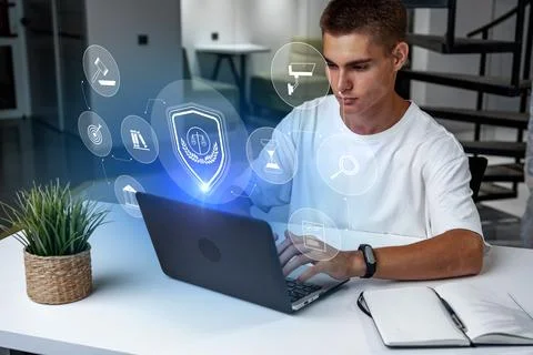 Young man using laptop with digital security icons in modern workspace 스톡 사진