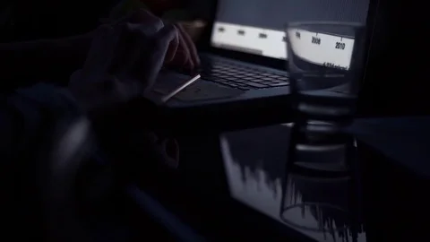 Young man using laptop in kitchen in evening. Glass of water and pencil on table Stock Footage 82938444