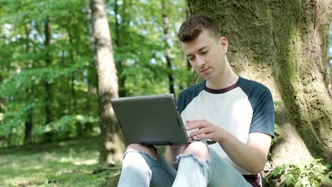 Young man using laptop in the park and smiling to the camera, steadycam shot Stock-Footage 76386412