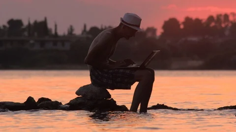 Young man using laptop on seashore. Freelance concept. Technology and travel Stock Footage 113511097