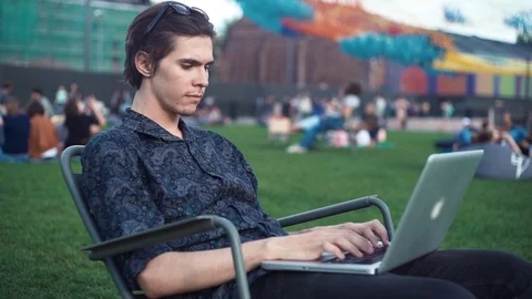 Young man using laptop sitting on chair at city park. Summer day Stock Footage 79356867