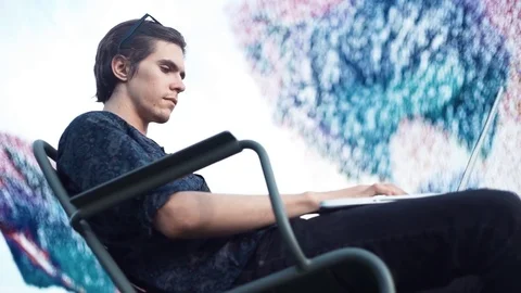 Young man using laptop sitting on chair outdoors. Summer day Video stock 79356932