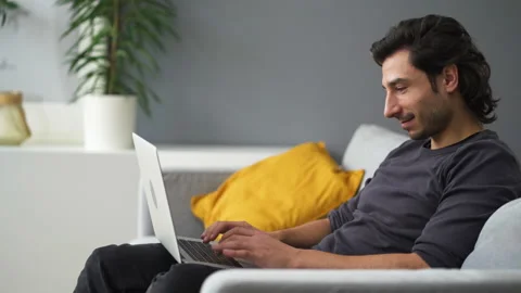 Young man using laptop sitting on the sofa at home Stock Footage 149242501