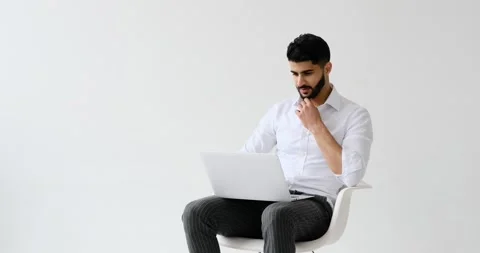 Young man using laptop sitting against white background Stockbeeldmateriaal 196078807