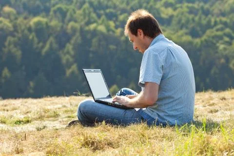 Young man using laptop sitting on the grass on the hillside Stock Photos