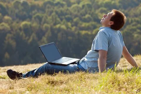 Young man using laptop sitting on the grass on the hillside Foto stock