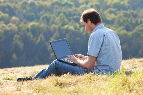 Young man using laptop sitting on the grass on the hillside Stock Photos