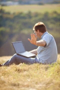 Young man using laptop sitting on the grass on the hillside Stock Photos
