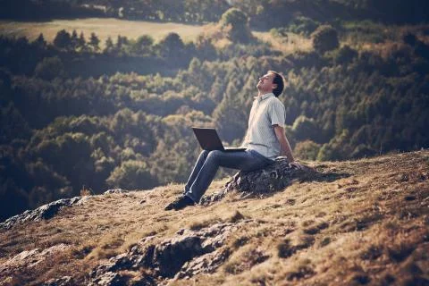 Young man using laptop sitting on the grass on the hillside Stock Photos