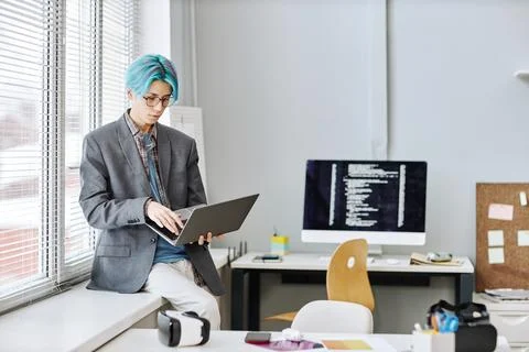 Young man using laptop sitting by window in office 库存照片