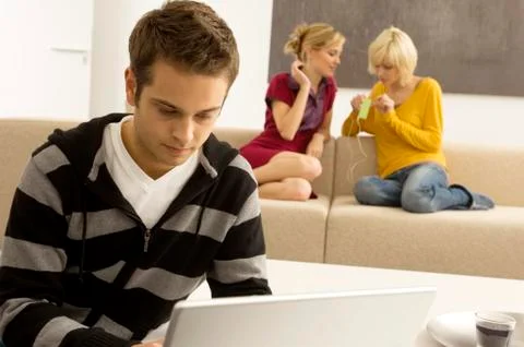 Young man using a laptop with two young women listening to an MP3 player in the Stock Photos
