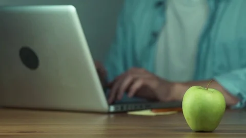 Young man using a laptop typing a message. Green apple on the table. Stock Footage 81882311