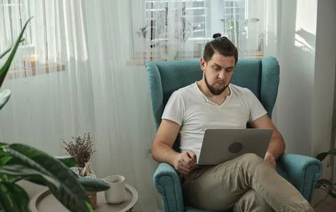 Young man using laptop typing and working sitting on the armchair at home Stock Photos