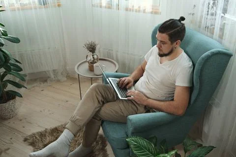 Young man using laptop typing and working sitting on the armchair at home Stock Photos