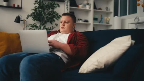 Young man using laptop while sitting on sofa, sedentary lifestyle, freelancer Video stock 249212469
