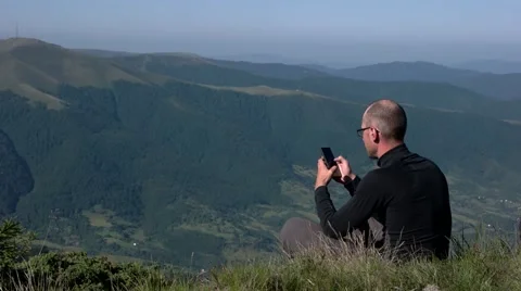 Young Man Using a Mobile Phone on a Mountain Top With Landscape Background Stock Footage 65420357