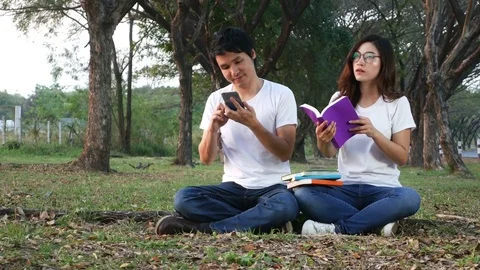 Young man using mobile phone and a woman reading a book in the park Video stock 85317700