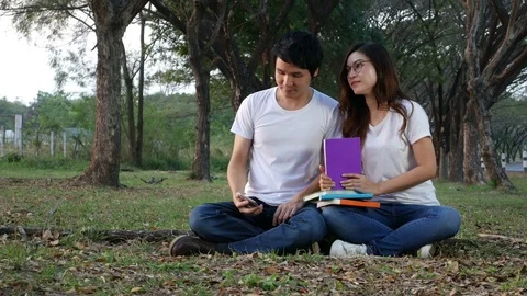 Young man using mobile phone and a woman reading a book in the park Stock-Footage 85318286