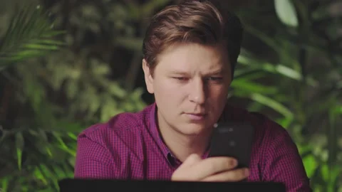 A young man using a mobile phone while sitting at a computer Stock Footage 150154789