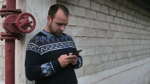 A young man using a mobile phone reads a telephone message or downloads an Stock Footage 218327193