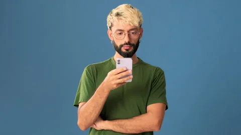 Young man using a mobile phone, isolated on blue background in a studio Stock Footage 302115956