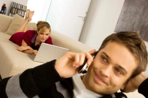 Young man using a mobile phone with a young woman using a laptop in the Stock Photos