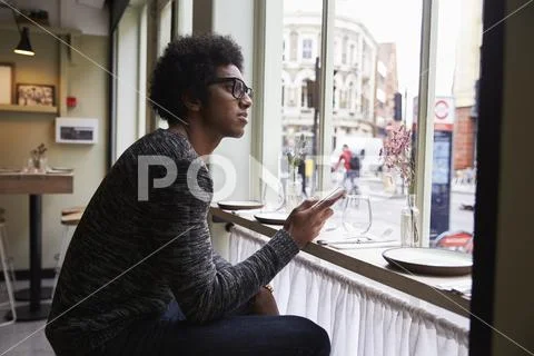 Young Man Using Mobile Phone To Update Social Media In Cafe Stock Photos