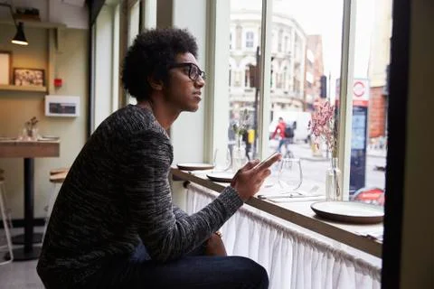 Young Man Using Mobile Phone To Update Social Media In Cafe Stock Photos