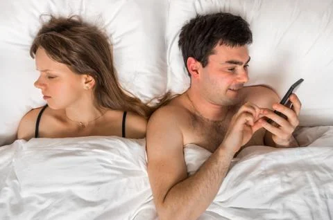 Young man using mobile phone, while his wife sleep at night - insomnia and ch Stock Photos