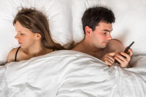 Young man using mobile phone, while his wife sleep at night - insomnia and ch Stock Photos