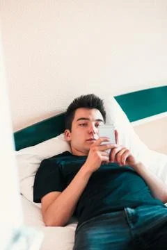 Young man using mobile phone laying in bed in bedroom Stock Photos