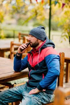 A young man using a mobile phone is sitting outdoors in a cafe or restaurant on Stock-Fotos