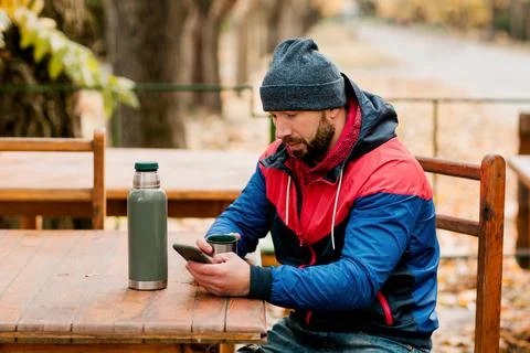 A young man using a mobile phone is sitting outdoors in a cafe or restaurant on Foto stock