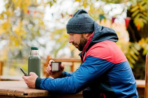 A young man using a mobile phone is sitting outdoors in a cafe or restaurant on Stock Photos