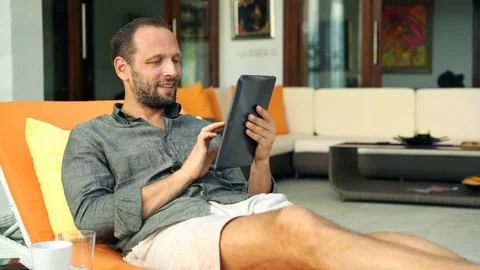 Young man using modern laptop while lying on sunbed at home, 4K Stock Footage 76056039