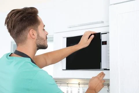 Young man using modern microwave oven at home Stock Photos