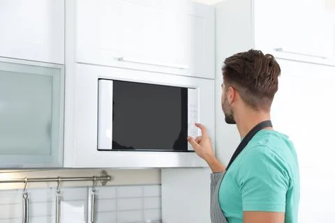 Young man using modern microwave oven at home Stock Photos