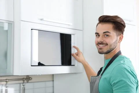 Young man using modern microwave oven at home Stock Photos