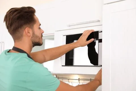 Young man using modern microwave oven at home Stock Photos