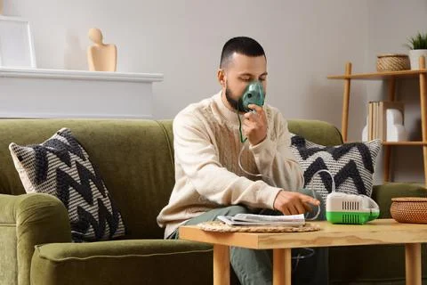 Young man using nebulizer on sofa at home Stock Photos