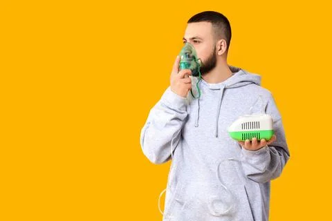 Young man using nebulizer on yellow background Stock Photos