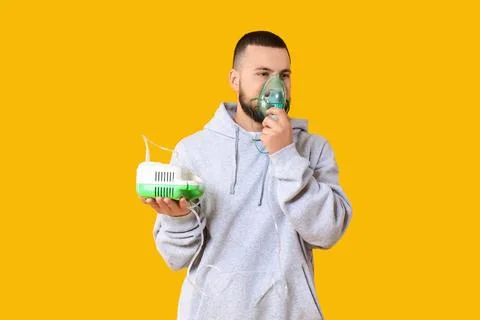 Young man using nebulizer on yellow background Stock Photos