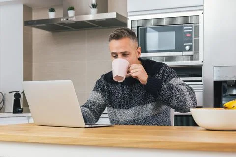 Young man using notebook while having breakfast, reading, writing email or wo Stock Photos